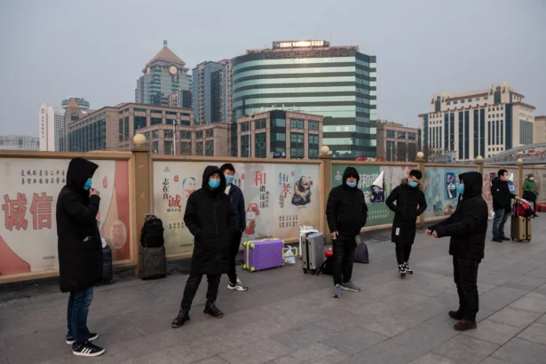 People wearing masks wait next to their suitcases at a railway station in Beijing on Jan. 27, 2020. (Nicolas Asfouri/AFP via Getty Images)