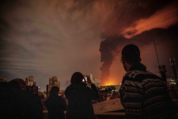 Residents watch and take pictures as flames and smoke rise from an oil storage facility struck as attacks hit the city during the U.S.–Israeli military campaign in Tehran, Iran, on March 7, 2026. (Alireza Sotakbar/ISNA via AP)