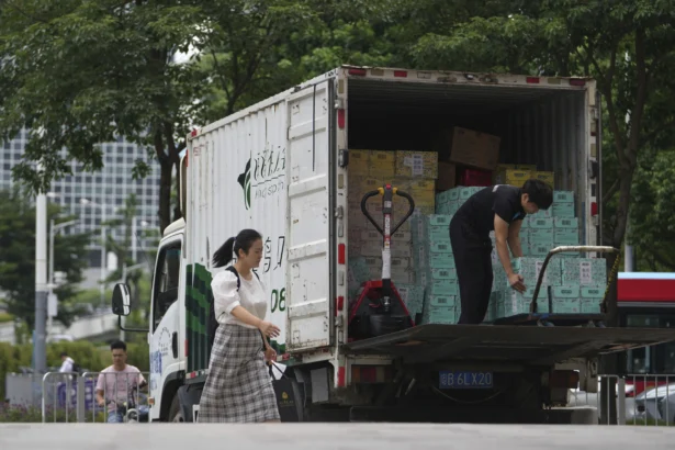 A woman walks past a worker unloading boxes of beverages from a truck in the Shenzhen Bay commercial district in Shenzhen, Guangdong province, China, on Sept. 19, 2025. (Andy Wong/AP Photo)